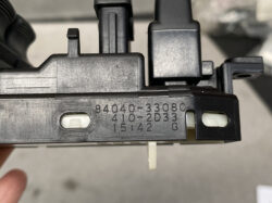 Close-up of a black plastic automotive mounting module with stamped part numbers visible (e.g., 84040-3080, 410-2D33).