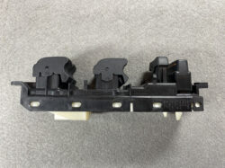 Automotive power window switch assembly on a black plastic mounting rail, with multiple button housings and white actuator clips.