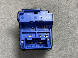Close-up of a blue automotive electrical connector housing with metal pin terminals visible in multiple sockets.
