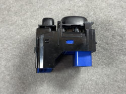 Close-up of a black plastic module with blue accents and a blue rectangular tab, on a gray surface (likely a modular switch/connector component).