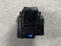 Black Toyota ABS brake module with a blue release tab on a gray surface.