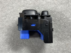 Compact black plastic mechanical module with a blue actuator/slide switch, viewed from the side on a gray surface.