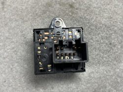 Close-up of a black automotive relay housing with multiple copper contact terminals and a metal mounting tab at the top, showing the internal connector block.