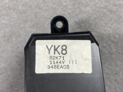 Close-up of a black electronic module with a beige label reading YK8, 82K71, 1144Y, 948EA05 and a mounting tab with a hole visible in the background.