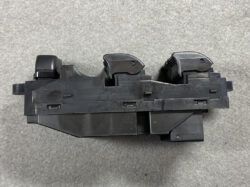 Black plastic mechanical assembly with two rounded top sections, lying on a gray surface; appears scratched and used.