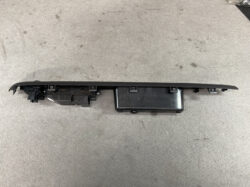 Long black car interior panel with mounting clips and a connected module, likely a dashboard switch assembly laid on a concrete floor