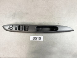 Driver-side car door panel showing power window switches, mirror control knob, and door lock button on a gray armrest panel