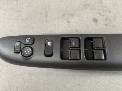 Driver-side door control panel with power window switches, a four-button auto window on the right, a window lock switch, and left-right mirror adjust pad with directional arrows