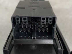 Close-up of a black automotive relay/fuse box with multiple terminal pins and connector slots.