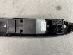 Close-up of a black automotive electronic control module with a multi-pin connector on the right and mounting screws, mounted on a plastic housing.