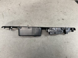 Long black automotive interior module with multiple mounting clips and electrical connectors, likely a center console or dash control unit structure.