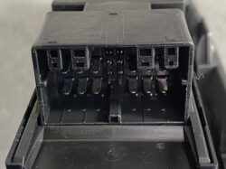 Close-up of a black plastic multi-pin electrical connector with several metal blade terminals and empty sockets.