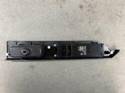 Black automotive door lock actuator module with electrical connector on a concrete surface, viewed from above