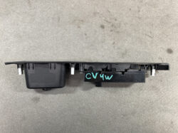 A black car window switch panel laid on a concrete floor, with multiple toggle levers and a turquoise 'CV4W' marking on the right side.