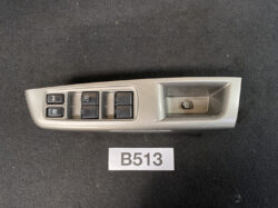 Interior car door panel with four power window switches, a window lock button, and a recessed door handle area on gray plastic.