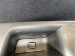 Close-up of a car interior door panel with a small latch and scratched plastic trim.