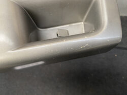Close-up of a gray car interior plastic panel with a small rectangular latch inside a recessed pocket and minor scratches/dirt.