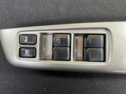 Driver-side power window control panel with four window switches and a window-lock button on a gray car door trim