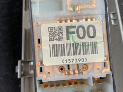 Close-up of a gray electrical module with copper contacts and a sticker showing a QR code, 'F00' text, a barcode, and the serial '(157390)'