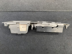 Detached car dashboard control module (gray plastic) with a beige label, lying on dark carpeted surface.