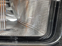 Close-up of a car headlight lens showing stamped certification marks (SAE, DOT) and part codes inside the clear plastic