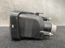 Black automotive electrical module with two bolt terminals and a gray plug-on connector, shown from the side on a dark surface.