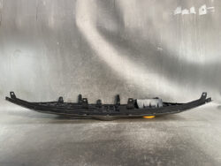 Curved black plastic automotive bumper support with multiple mounting brackets on a workshop surface