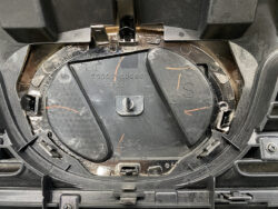 Close-up of a circular automotive mounting plate with a central screw and two curved covers, marked with 480 and S, surrounded by plastic clips and housings.
