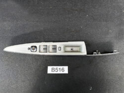 Side view of a gray car door interior panel with power window controls and lock switch on a dark surface like a workshop item