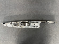 Gray plastic automotive control module with an electrical connector block and multiple mounting clips, laid on a dark textured surface.