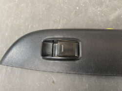 Close-up of a black rectangular switch embedded in a textured car interior panel, shown from above.