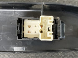 Close-up view of a beige multi-pin electrical connector housed in black plastic, with metal contact points visible inside a vehicle-style receptacle