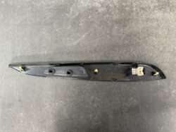 Long black automotive interior trim panel with two circular holes, yellow mounting clips, and a beige electrical connector at the end.