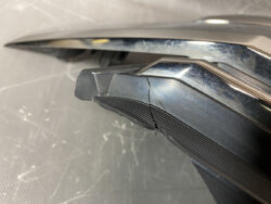 Close-up of a cracked black plastic hinge on a device with a chrome metal trim, showing a diagonal fracture and scuff marks.
