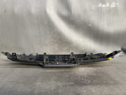 Long black car bumper cover fragment with mounting clips laid on a workshop surface, likely a damaged or spare automotive trim piece