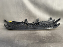 Long black automotive bumper cover/trim piece laid on a studio surface, showing mounting clips and tabs for installation on a vehicle's bumper core rail.