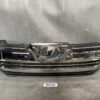 Front grille of a dark chrome Lexus with emblem in the center, resting on a workshop surface. TOYOTA VELLFIRE ANH20 Front Grille 53101-58140 53101-58150 » JDM-PARTS NZ