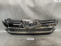 Front grille of a dark chrome Lexus with emblem in the center, resting on a workshop surface.