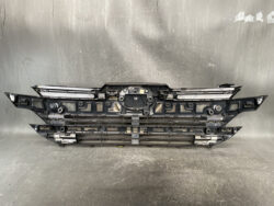 Front bumper assembly panel laid on a gray surface, showing mounting points and grille inserts for a vehicle front end.