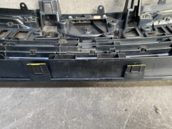 Close-up of a black plastic automotive interior part with multiple mounting tabs and clips on a textured workbench surface.