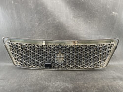 Chrome honeycomb front grille from a car, with mounting tabs and a central badge area.