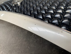 Close-up of a car grille with black pyramid-shaped inserts and a light gray bumper showing paint chips.