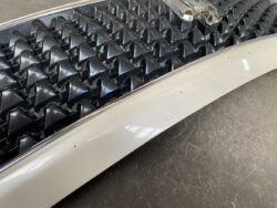 Close-up of a vintage car grille with black pyramid-shaped teeth and a chrome badge above a light gray bumper.