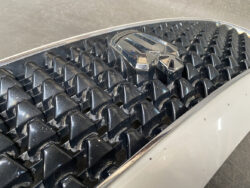 Close-up of a black honeycomb car grille with a chrome emblem resting on top of the grille trim.