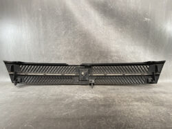 Front bumper grille for a vehicle, black with honeycomb mesh and central mounting area on a workshop surface.