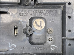 Close-up of a dirty Toyota engine bay panel featuring a circular beige cap with a black latch, two visible screws, and 'ABS TOYOTA' markings.