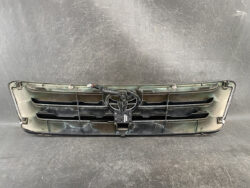 Front car grille assembly with a central Toyota emblem, showing wear and grime on a dark background.