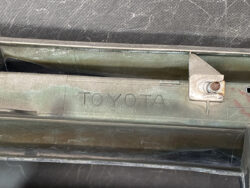 Metal car interior panel with the word TOYOTA embossed in the metal, showing a rusted bolt and greenish grime along the edge.