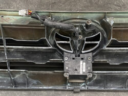 Close-up of a dusty car front showing a central grille area, with a black mounting plate bolted to the bumper and exposed wiring above it.