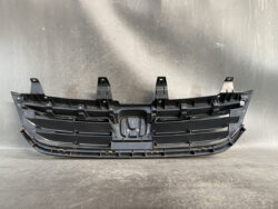 Black plastic front grille assembly for a vehicle, with mounting brackets, laid on a gray surface.